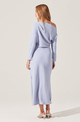A woman is wearing a light blue, long-sleeved, off-the-shoulder dress with a loose, draped top and a fitted waist. The dress has a silky, flowing fabric and reaches down to her ankles. She is wearing beige high-heeled sandals.